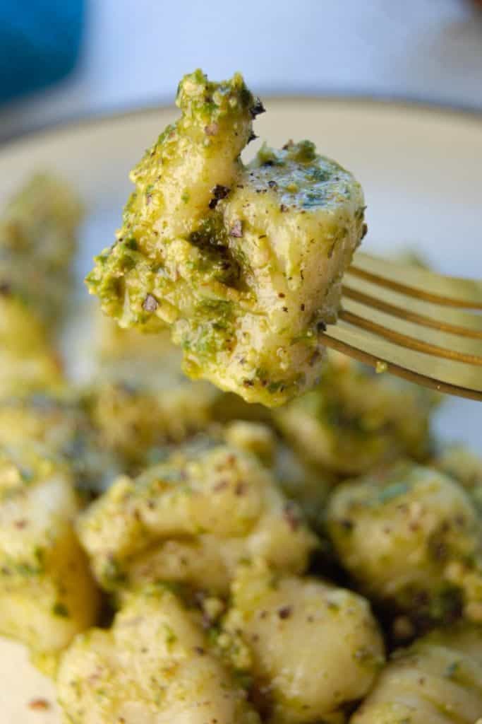 Two homemade vegan gnocchis in pesto sauce on a fork.