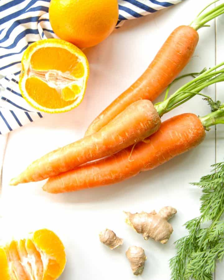 Ingredients for carrot orange juice with ginger on a marble counter.