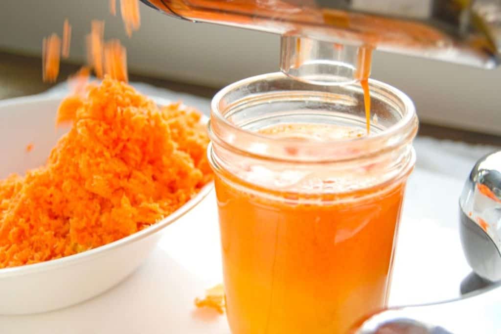 A juicer pouring out fresh carrot and orange juice.