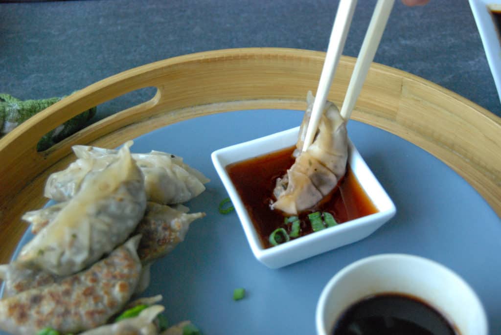 Chopsticks dipping a gyoza potsticker into chile oil.