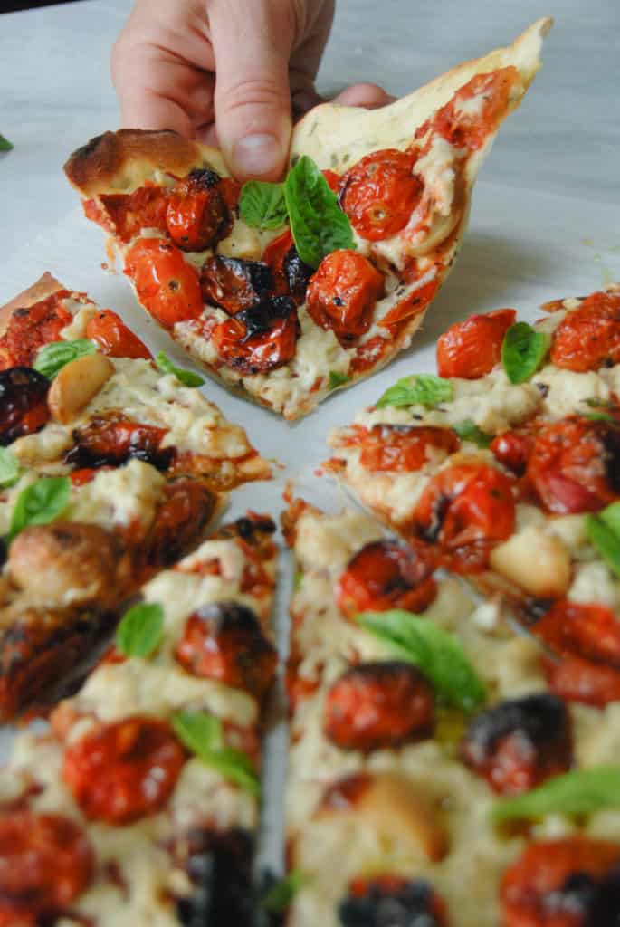 a hand grabbing a slice of vegan cheese pizza
