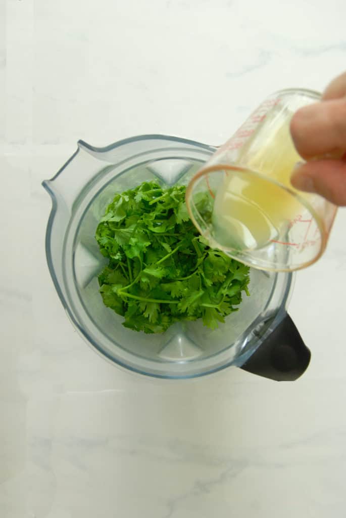 pouring lemon juice into a blender with chopped cilantro