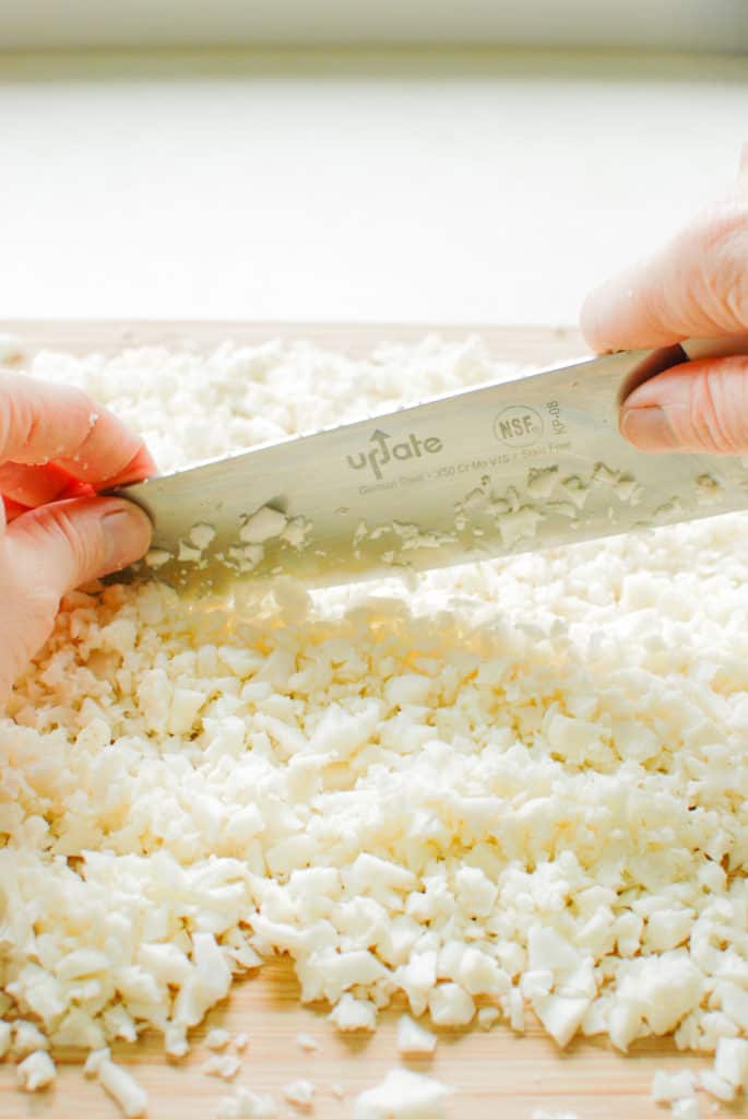 hands holding a chef's knife, cutting cauliflower into rice
