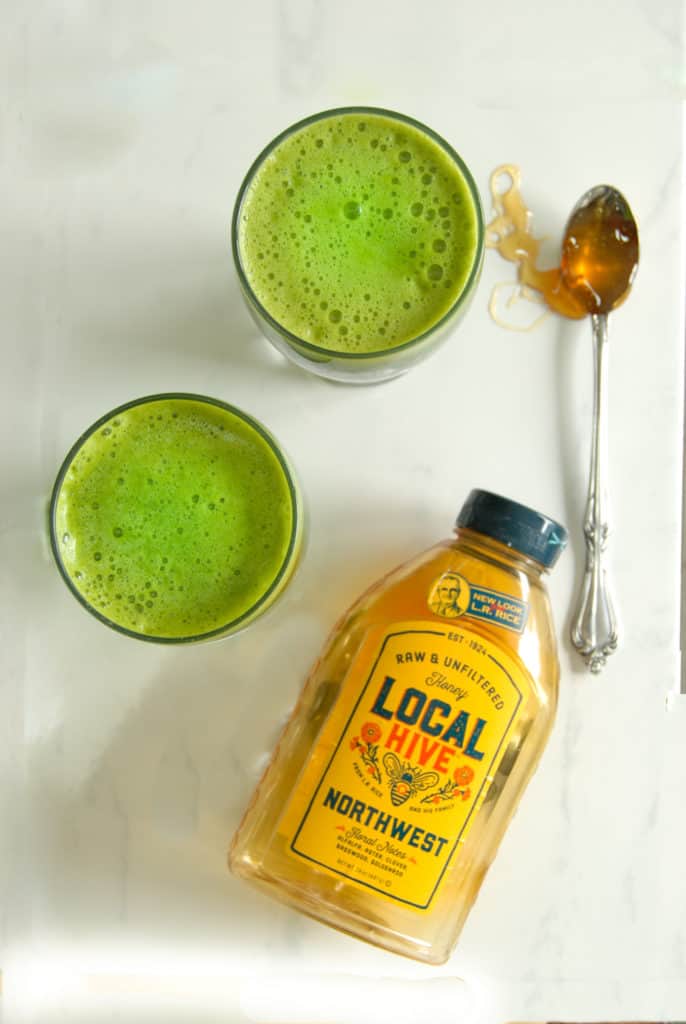 Two glasses of cilantro juice next to a bottle of local hive honey.