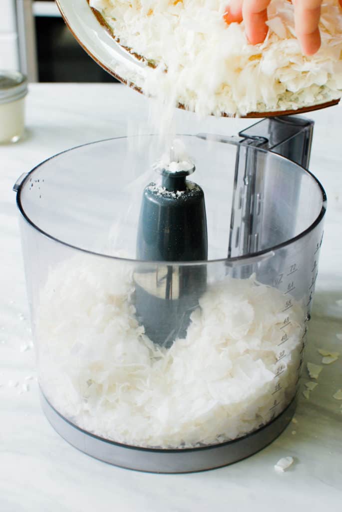 adding shredded coconut to a food processor
