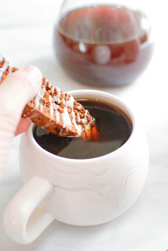 a hand dipping a pumpkin biscotti into coffee.