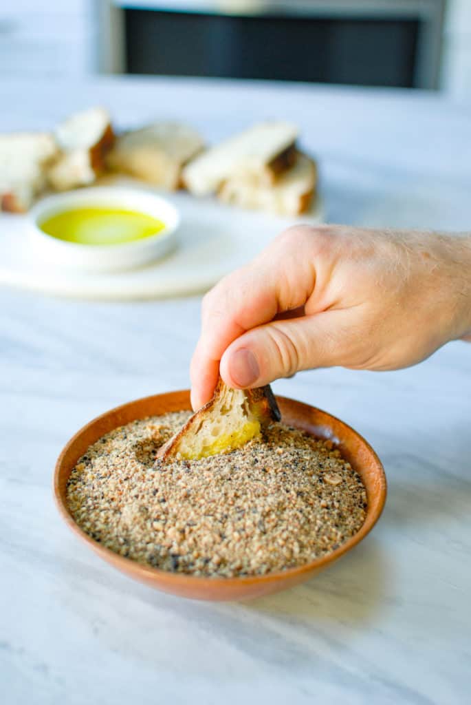 hand dipping a piece of crusty bread into willamette transplant's dukkah seasoning blend
