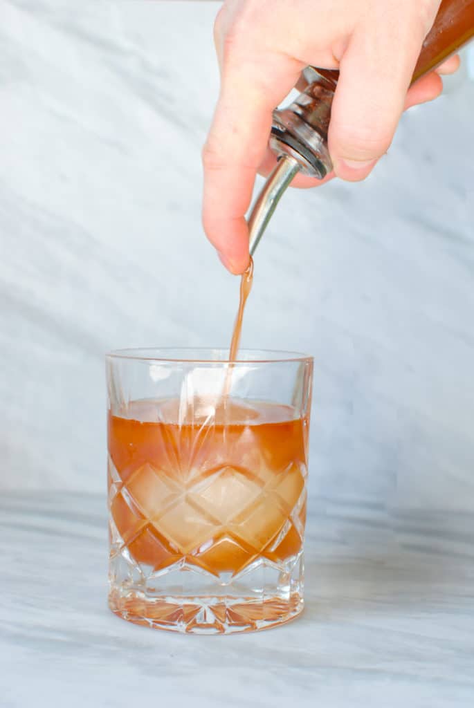 a hand pouring orgeat syrup into a cocktail.