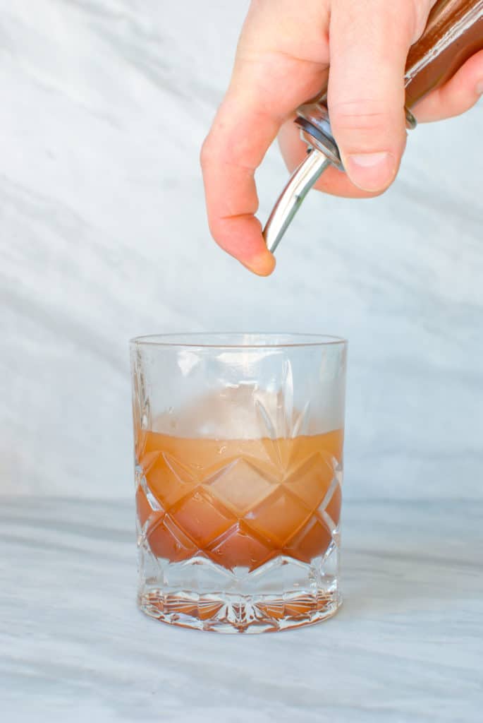 a hand pouring homemade orgeat into a glass.