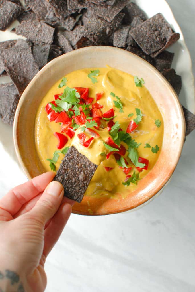 a hand dipping a chip into savory pumpkin queso