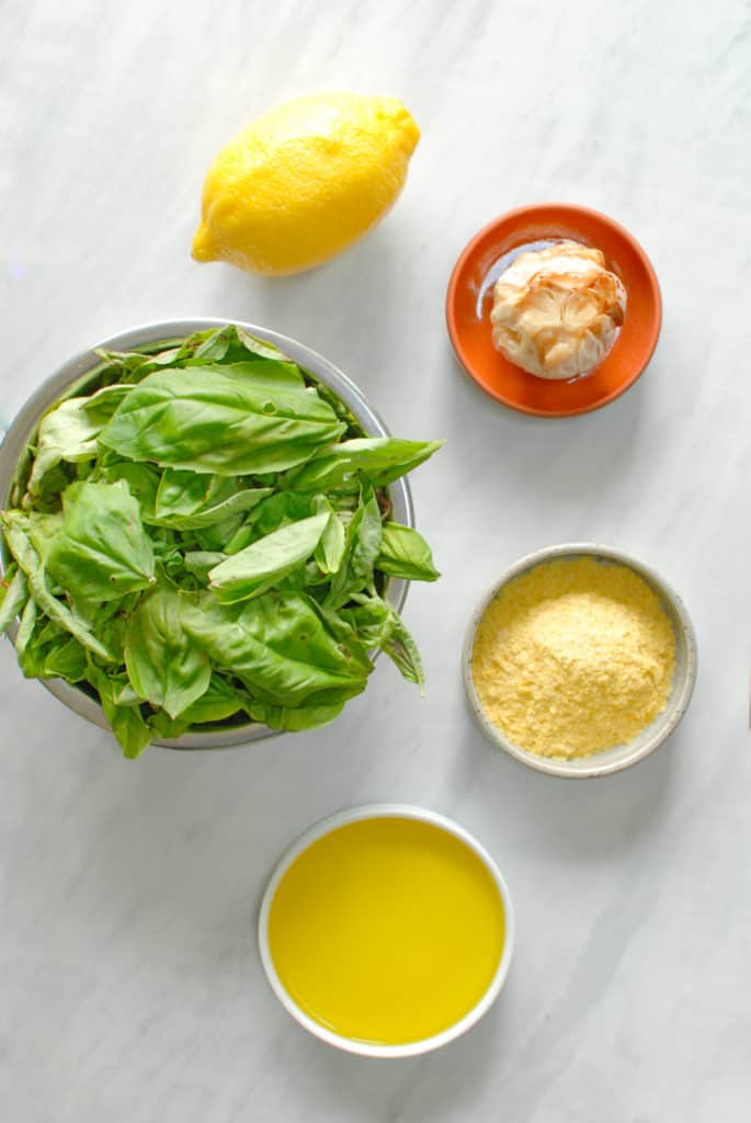 ingredients in bowls on a counter, ready to make roasted garlic pesto sauce.