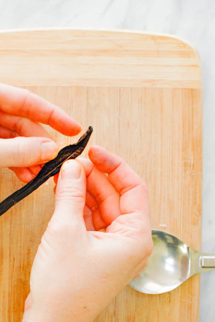 two hands splitting a vanilla bean pod open to reveal the vanilla seeds
