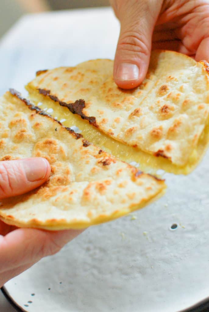 hand holding quesadilla and melty cheese pulling apart