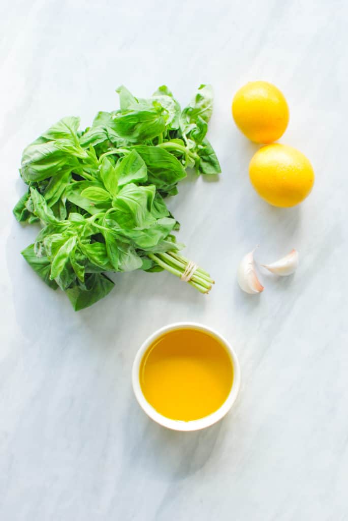 Ingredients to make meyer lemon pesto on a countertop: fresh basil, garlic, olive oil & meyer lemons!