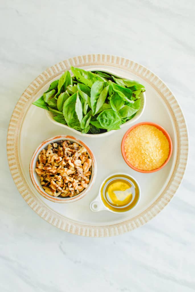 Fresh basil, toasted walnuts, olive oil, and nutritional yeast arranged on the counter.