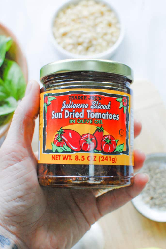 a hand holding a jar of sundried tomatoes to make pesto with