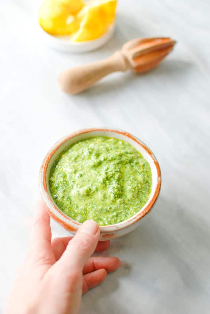 A hand reaching for a bowl of fresh meyer lemon pesto.