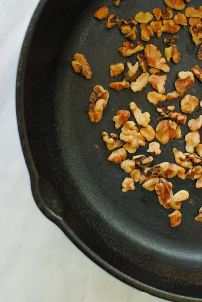 A cast iron pan with toasted walnuts to make vegan walnut pesto.