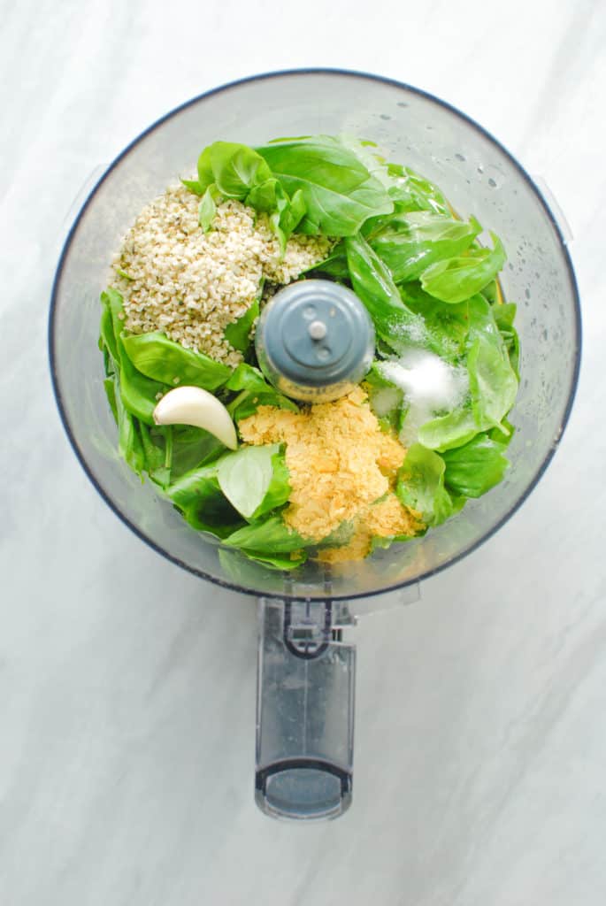 A food processor full of ingredients to make nut free pesto sauce.