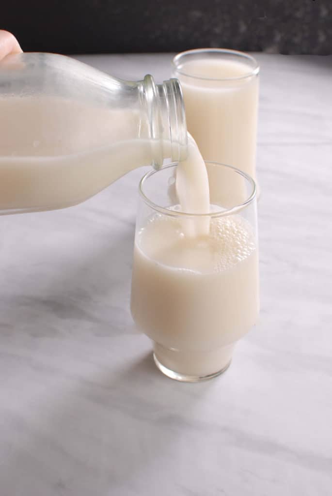 A jug pouring fresh flaxseed milk into a glass.