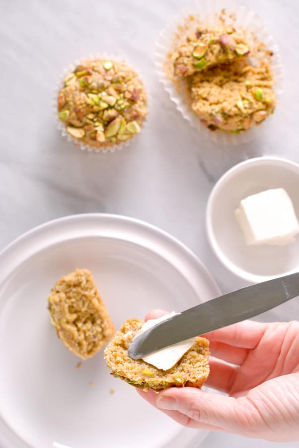 knife spreading butter on fresh pistachio muffins 