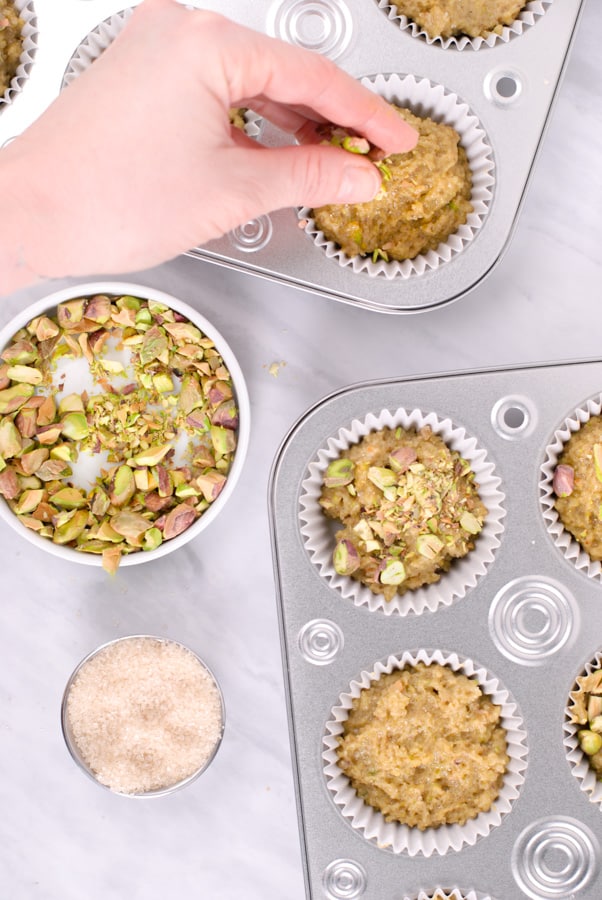 hand sprinkling chopped pistachios on top of muffins