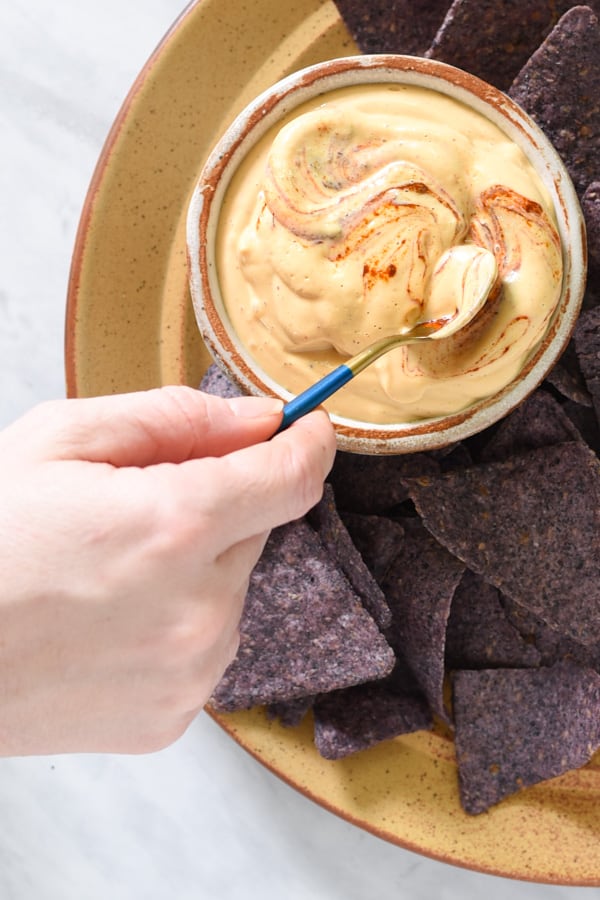 a spoon swirling chipotle peppers into nacho cheese