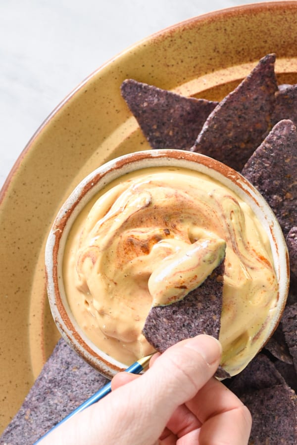 a hand dipping a chip into tofu nacho cheese sauce