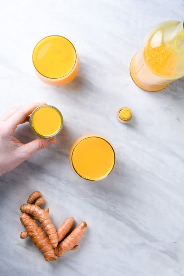 a hand reaching for a turmeric juice shot