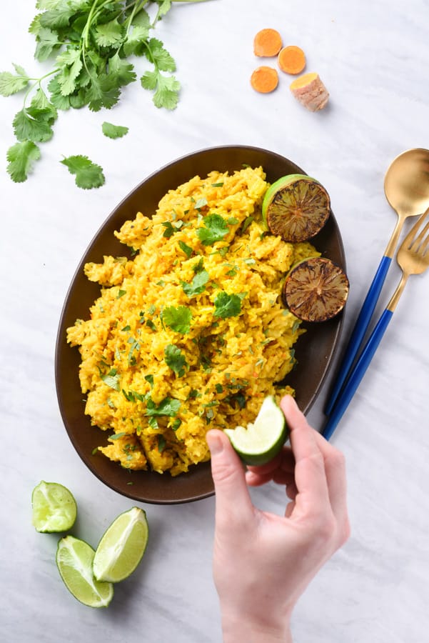 a hand squeezing lime on turmeric rice