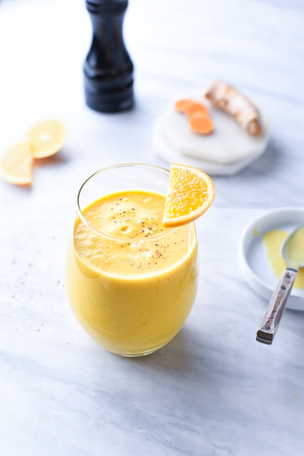 Turmeric smoothie on a marble counter with black pepper on top