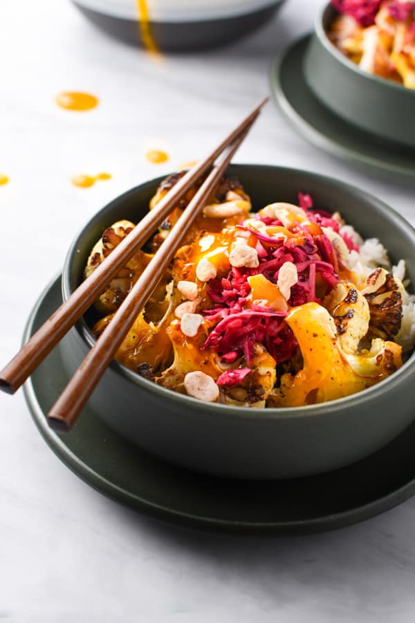 Chopsticks resting on a rice bowl with orange turmeric sauce