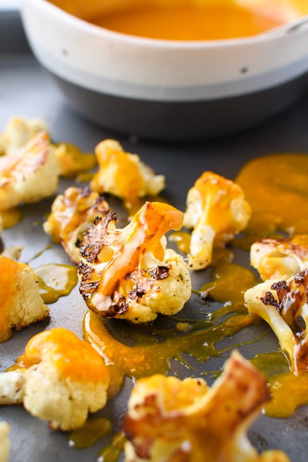 Roasted cauliflower drizzled with orange turmeric sauce on a sheet pan