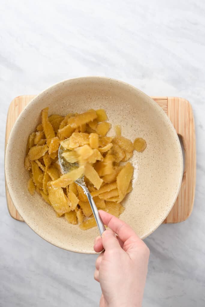 A hand with a spoon tossing candied ginger in sugar.