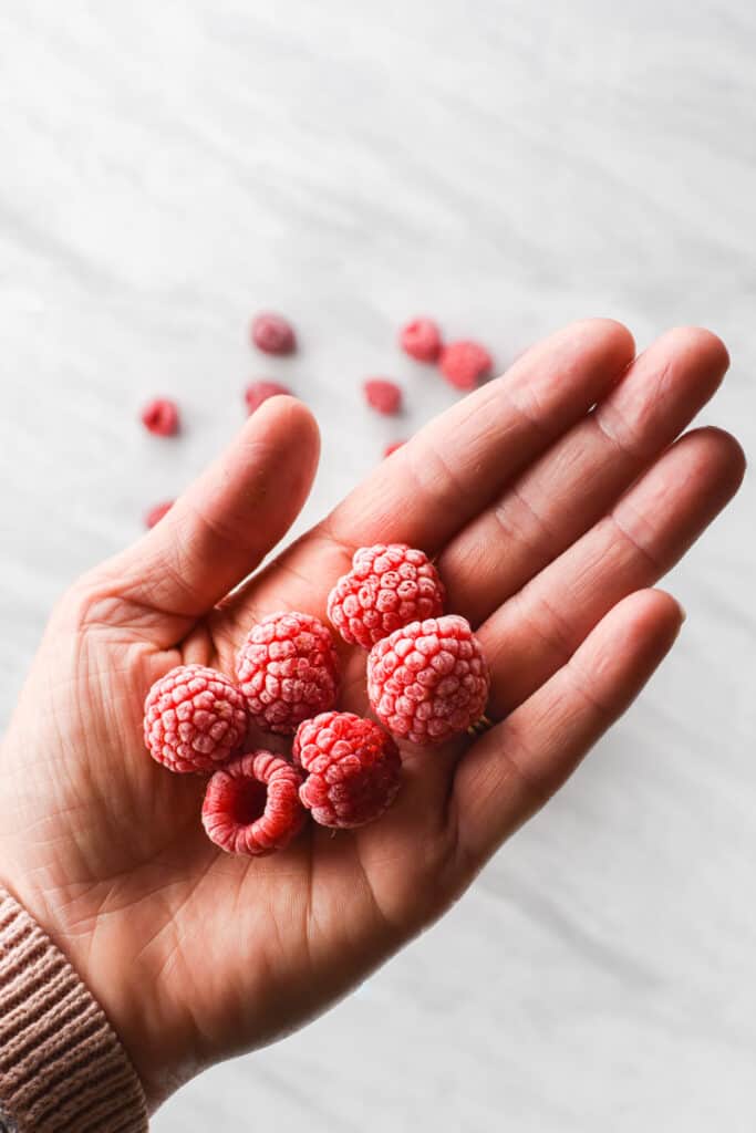 a hand holding frozen raspberries with a layer of frost on them