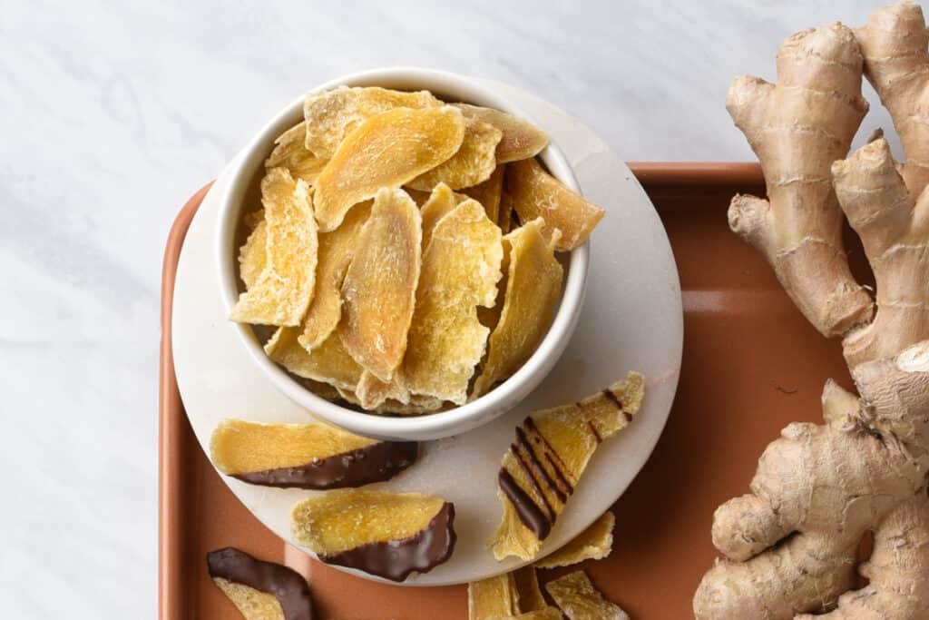 A bowl of chocolate drizzled candied ginger slices on the counter.