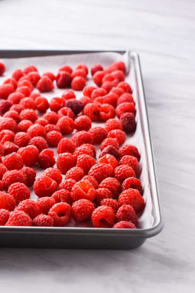 a baking sheet full of frozen raspberries