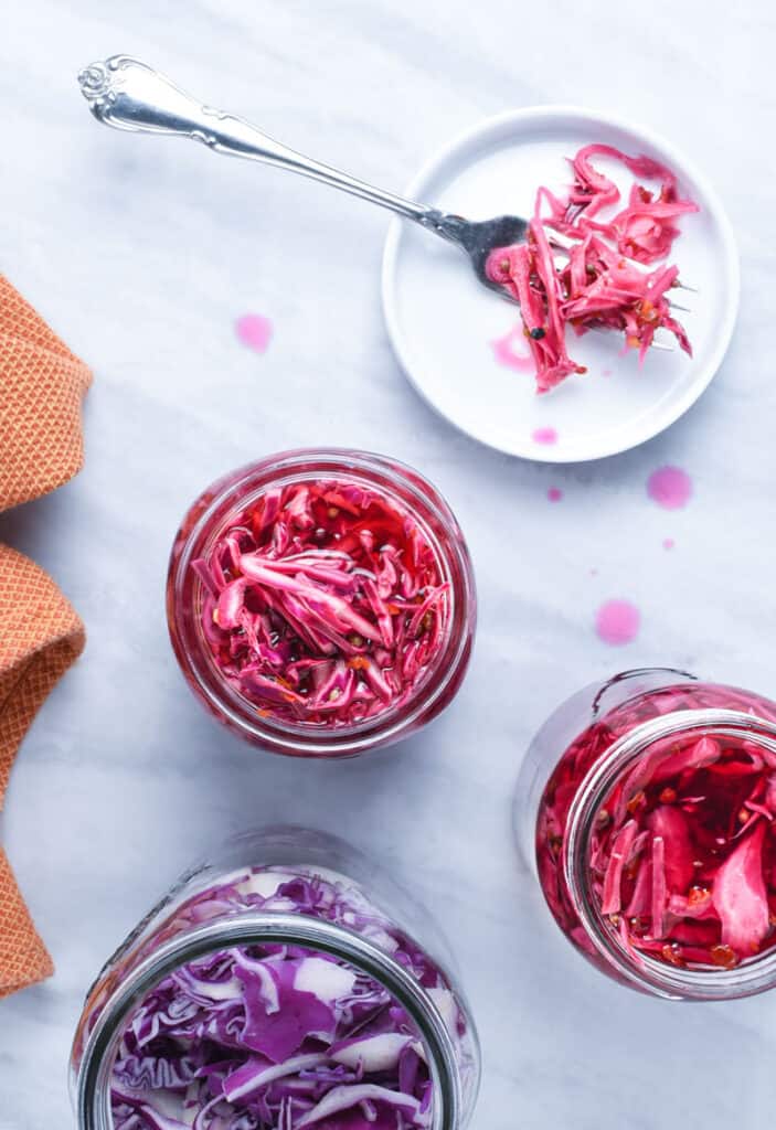 Three jars of homemade pickled red cabbage and some on a fork.