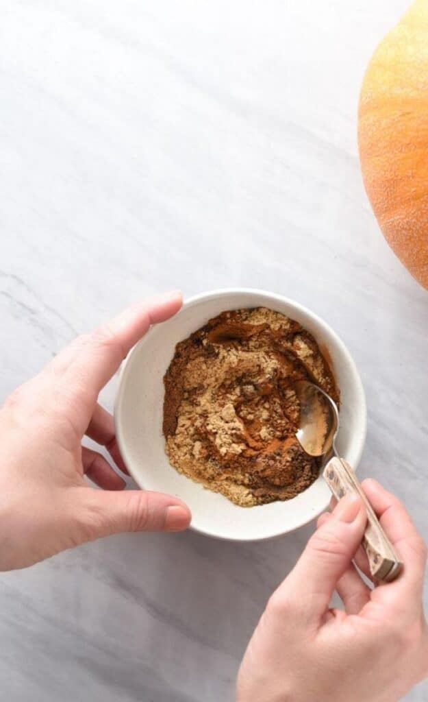 A hand stirring spices together to make homemade pumpkin pie spice.