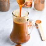 A spoon drizzling pumpkin spice syrup into a jar.