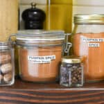 Jars of homemade pumpkin pie spice on a kitchen shelf.