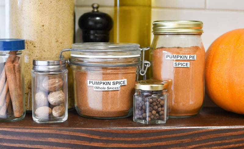 Jars of homemade pumpkin pie spice on a kitchen shelf.