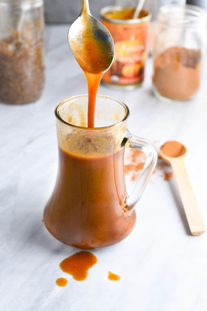 A spoon drizzling pumpkin syrup into a jar.