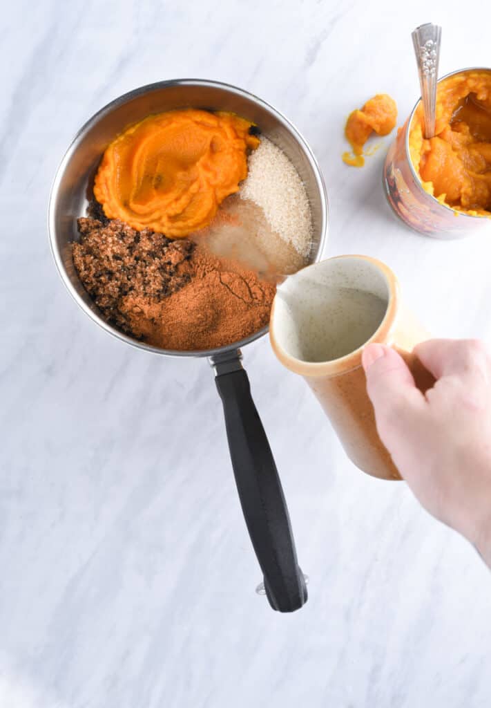 A hand pouring pumpkin spice syrup ingredients into a pot.