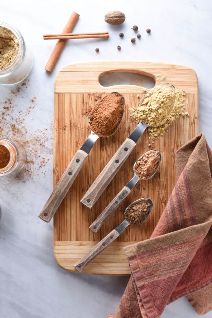 A cutting board with spices to make pumpkin spice: cinnamon, ginger, nutmeg, and allspice.