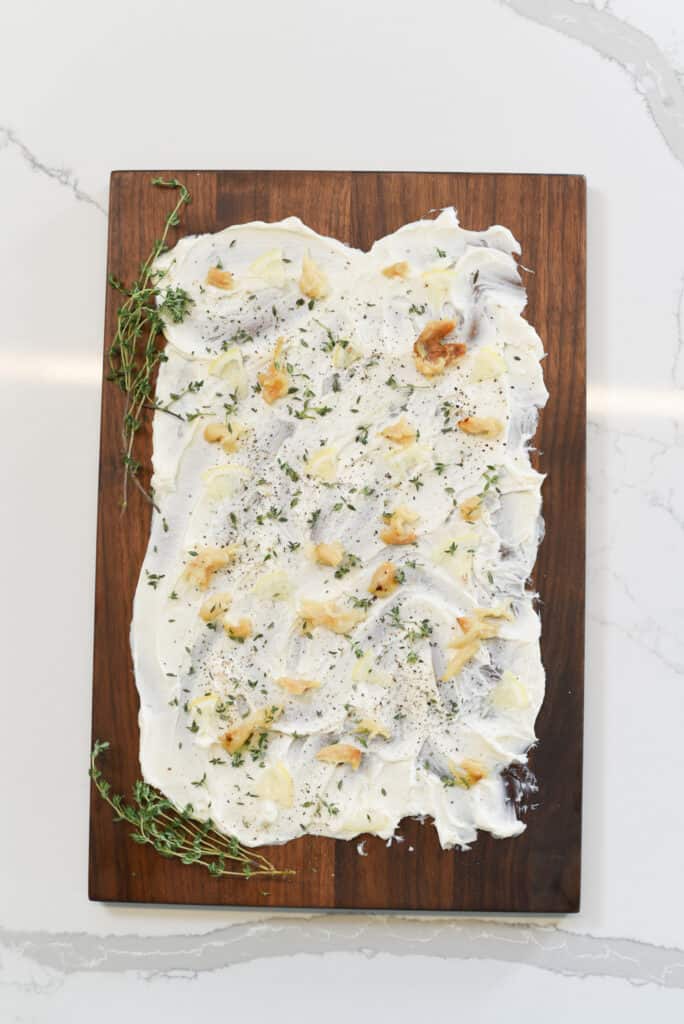 butter spread on a cutting board covered with fresh herbs and lemon slices