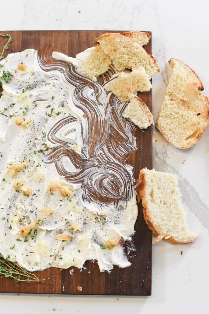 bread next to a cutting board layered with butter and fresh herbs.