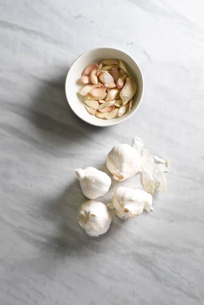 whole heads of garlic and a bowl of garlic cloves on the counter