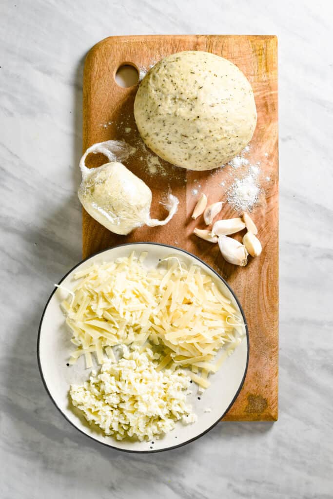 Ingredients to make garlic pizza on a cutting board.