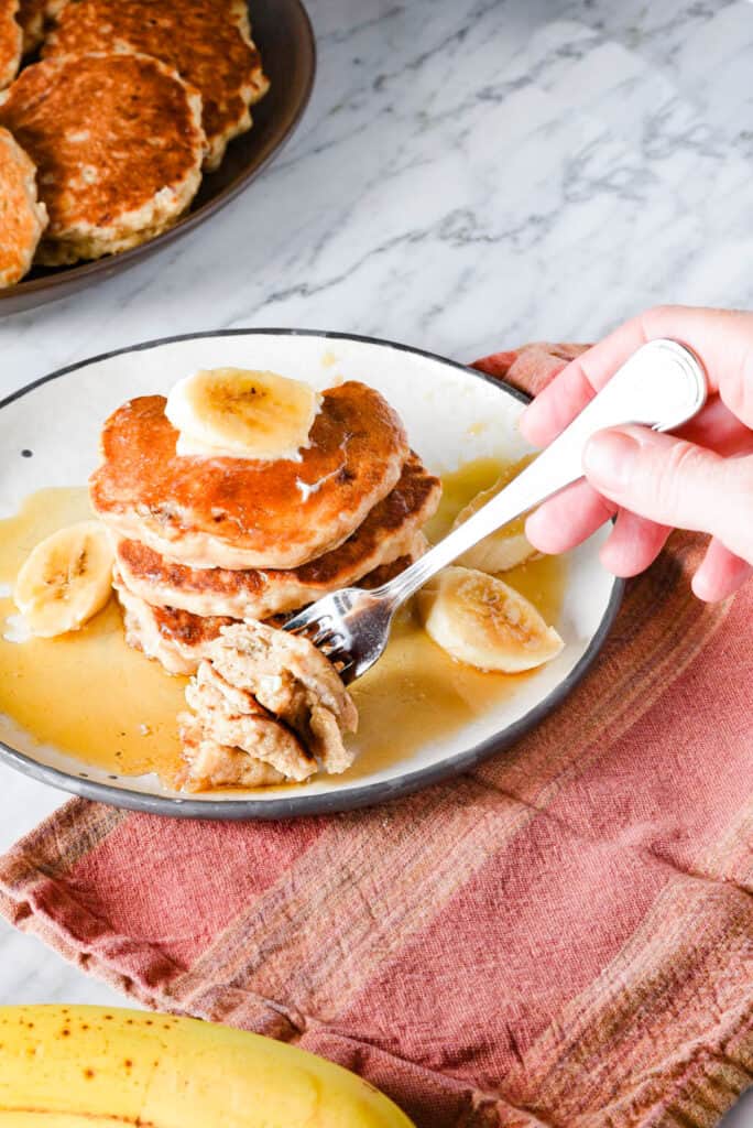 A fork cutting a bite out of a stack of vegan banana pancakes